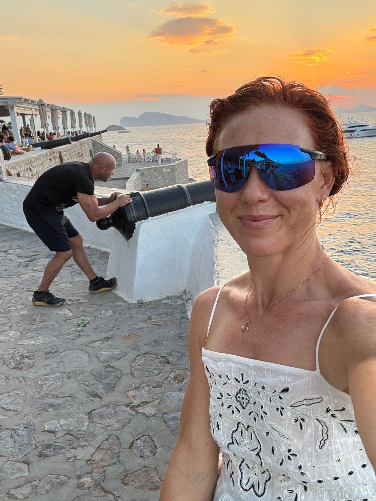 Selfie at sunset by the old cannons on the harbour walls of Hydra, with someone pushing a cannon in the background