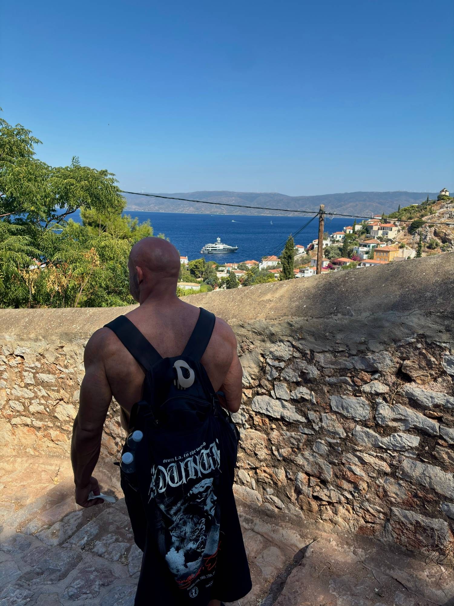 Walking up stone steps above Hydra Town with a view over the sea and a large yacht in the bay