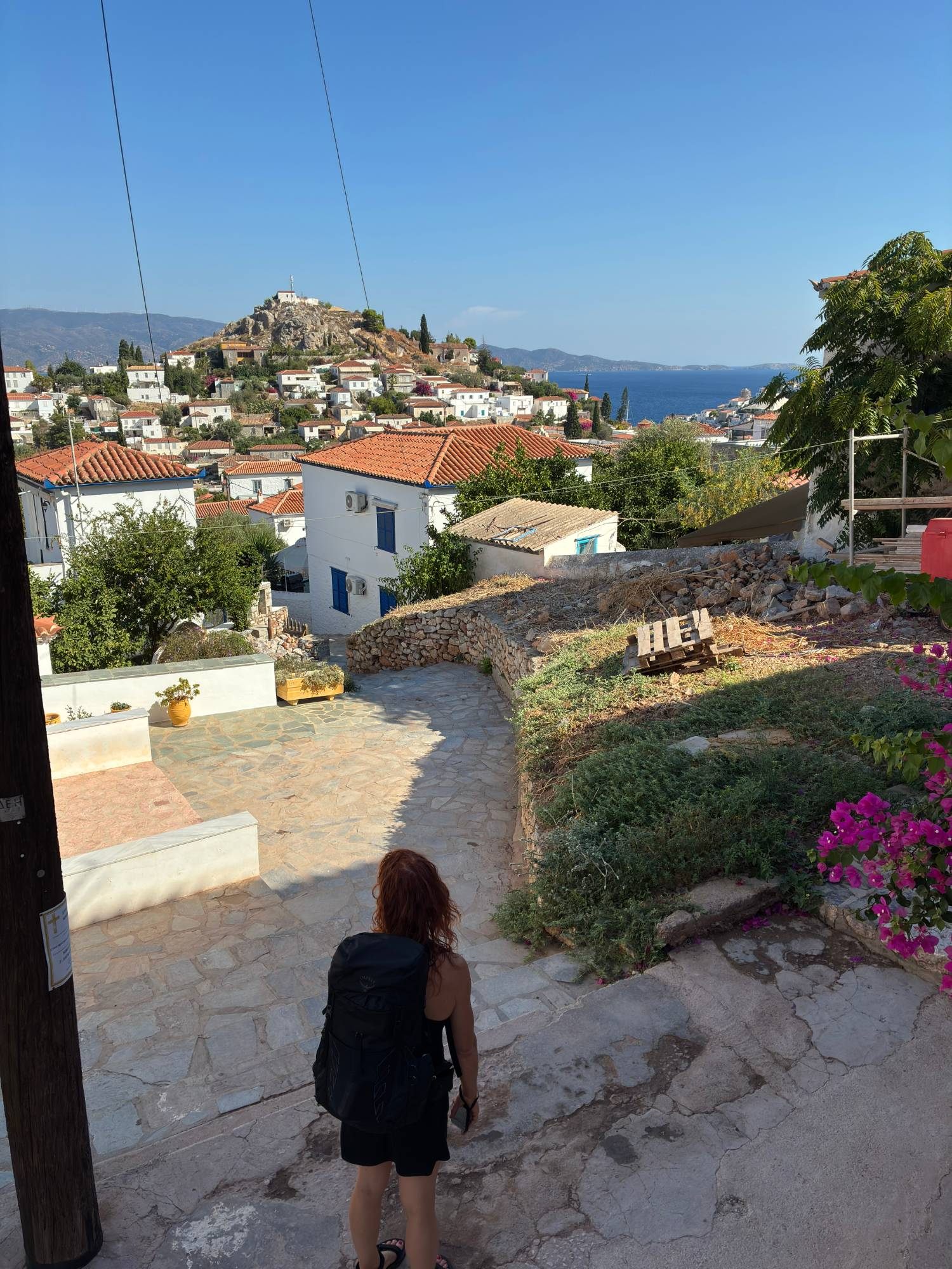 Kristine with a backpack looking down over the red roofs of Hydra Town towards the sea