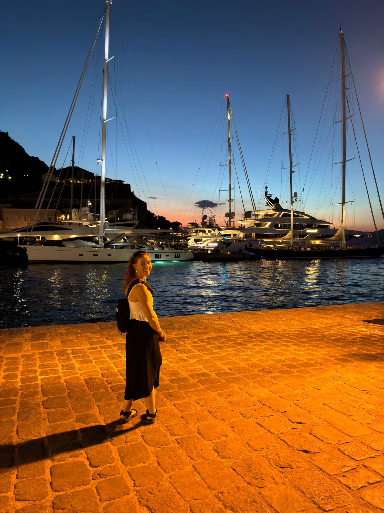 Kristine on the cobbled quay in front of large sailing yachts at blue hour in Hydra