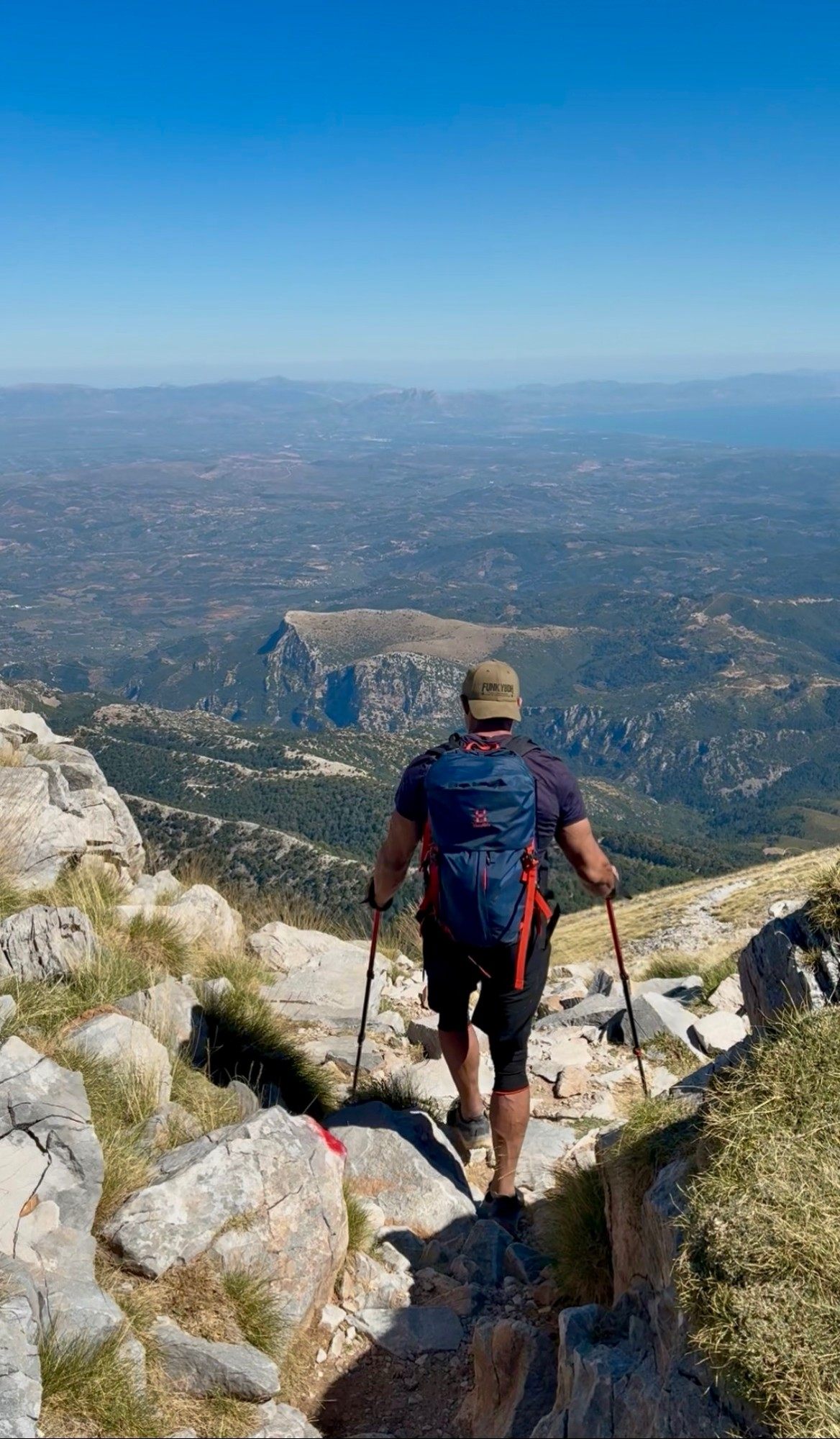 Hiking down the rocky upper trail of Mount Taygetos with trekking poles, looking out over Messenia and the sea