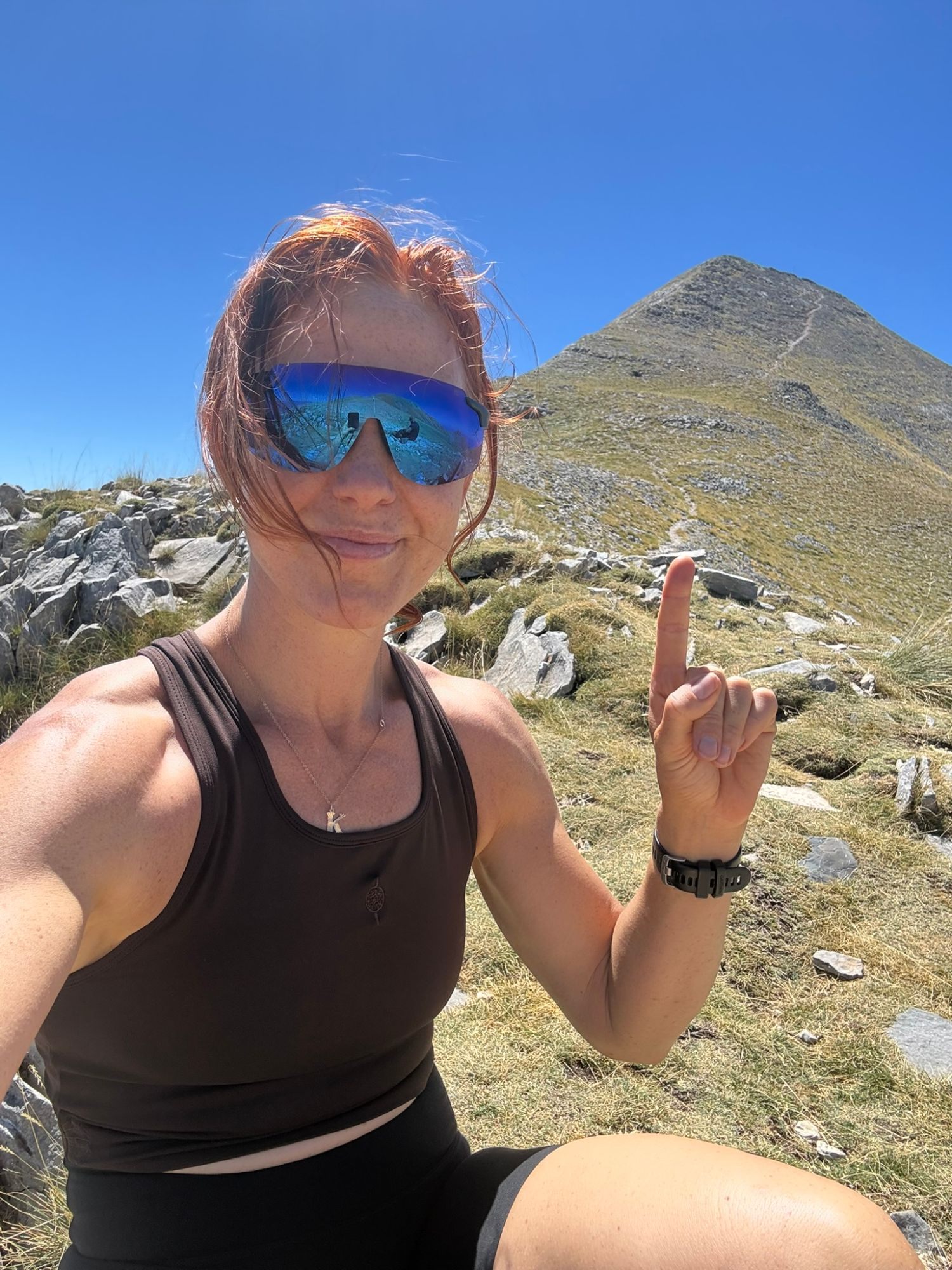 Kristine pointing up at the pyramid-shaped summit of Profitis Ilias with the trail zig-zagging up its flank