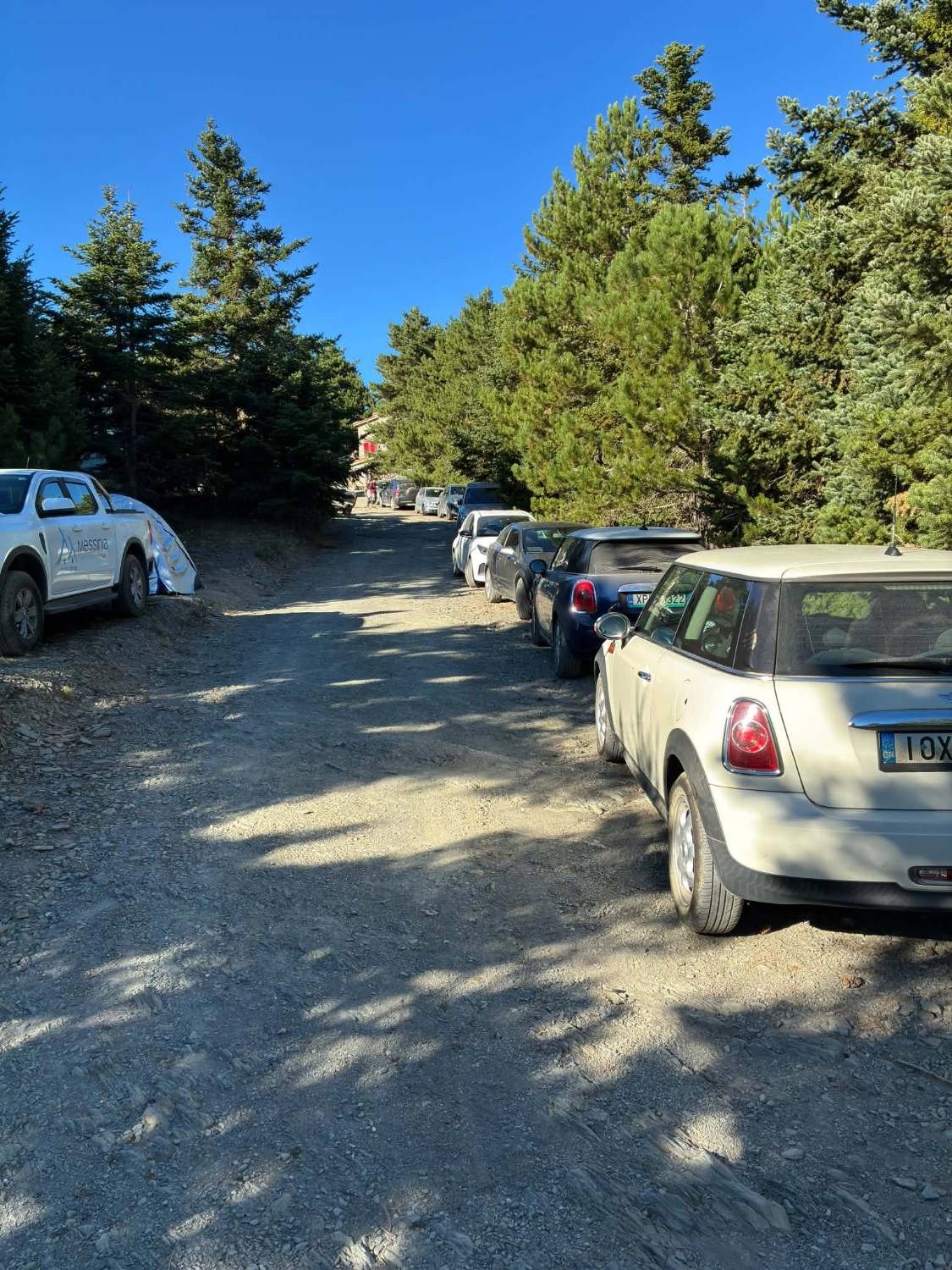 Small cars, including Mini Coopers, parked along the gravel road leading to the Taygetos Refuge