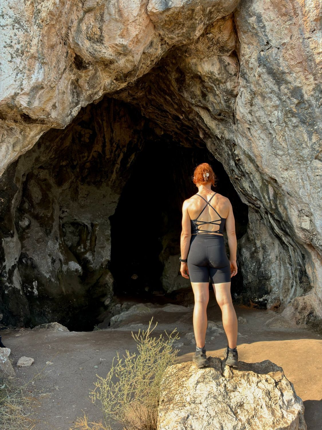 Kristine standing on a rock in front of the huge entrance to Nestor's Cave