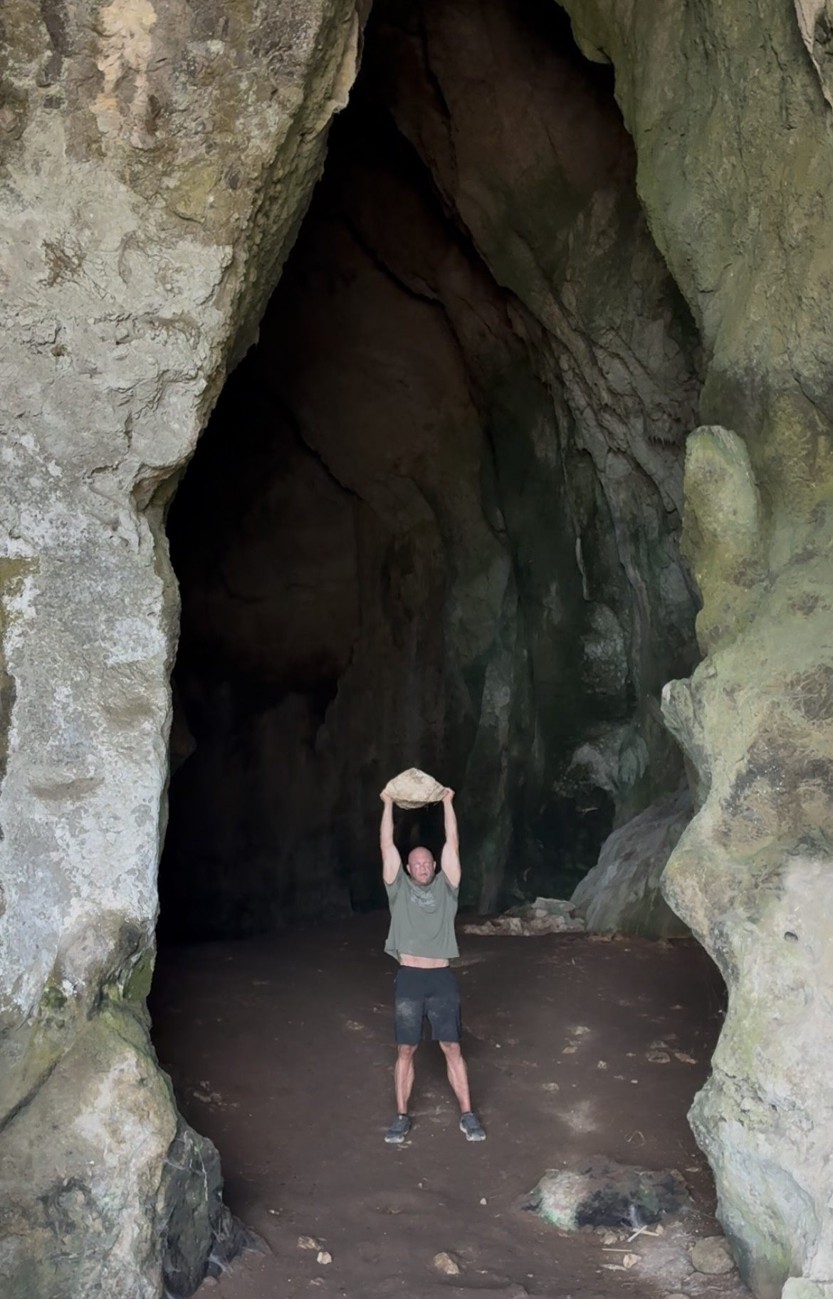 Lifting a rock overhead inside the huge entrance of Nestor's Cave