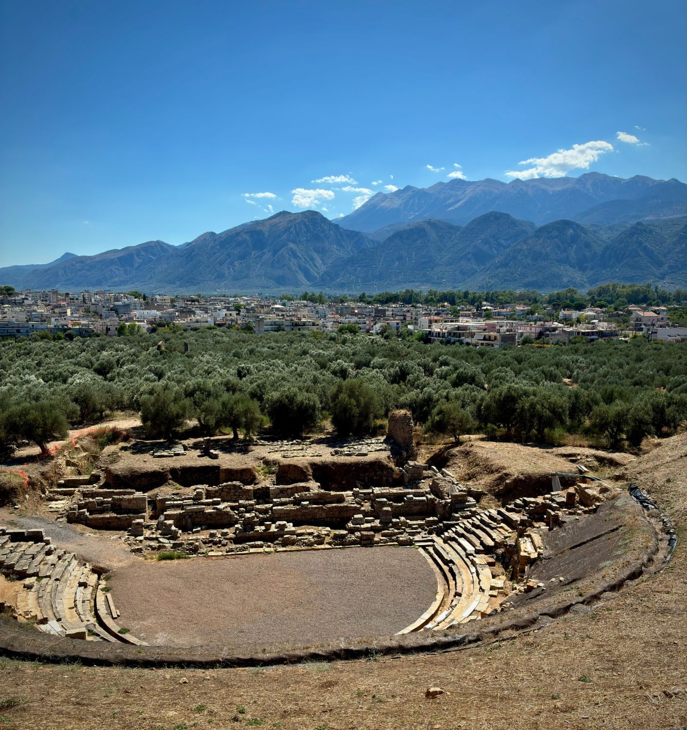 The ancient theatre of Sparta among olive groves, with the modern town and the Taygetos mountains behind