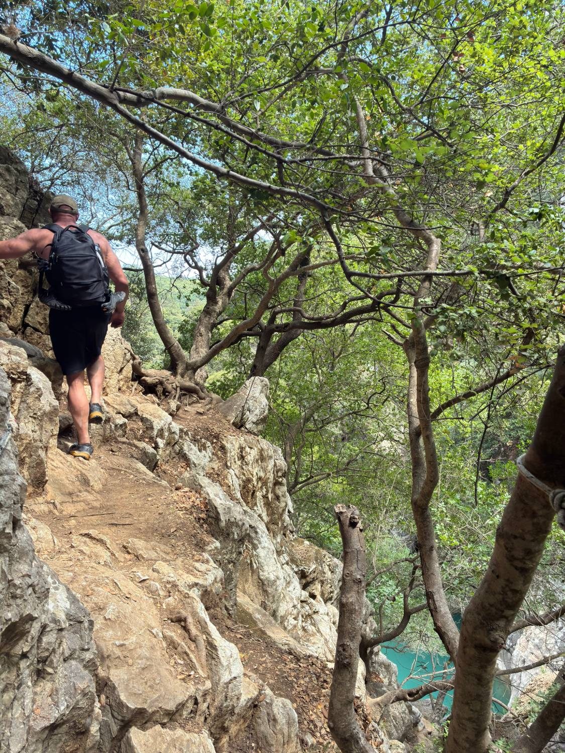 Walking a narrow rocky path along the cliff above a turquoise pool at Polylimnio