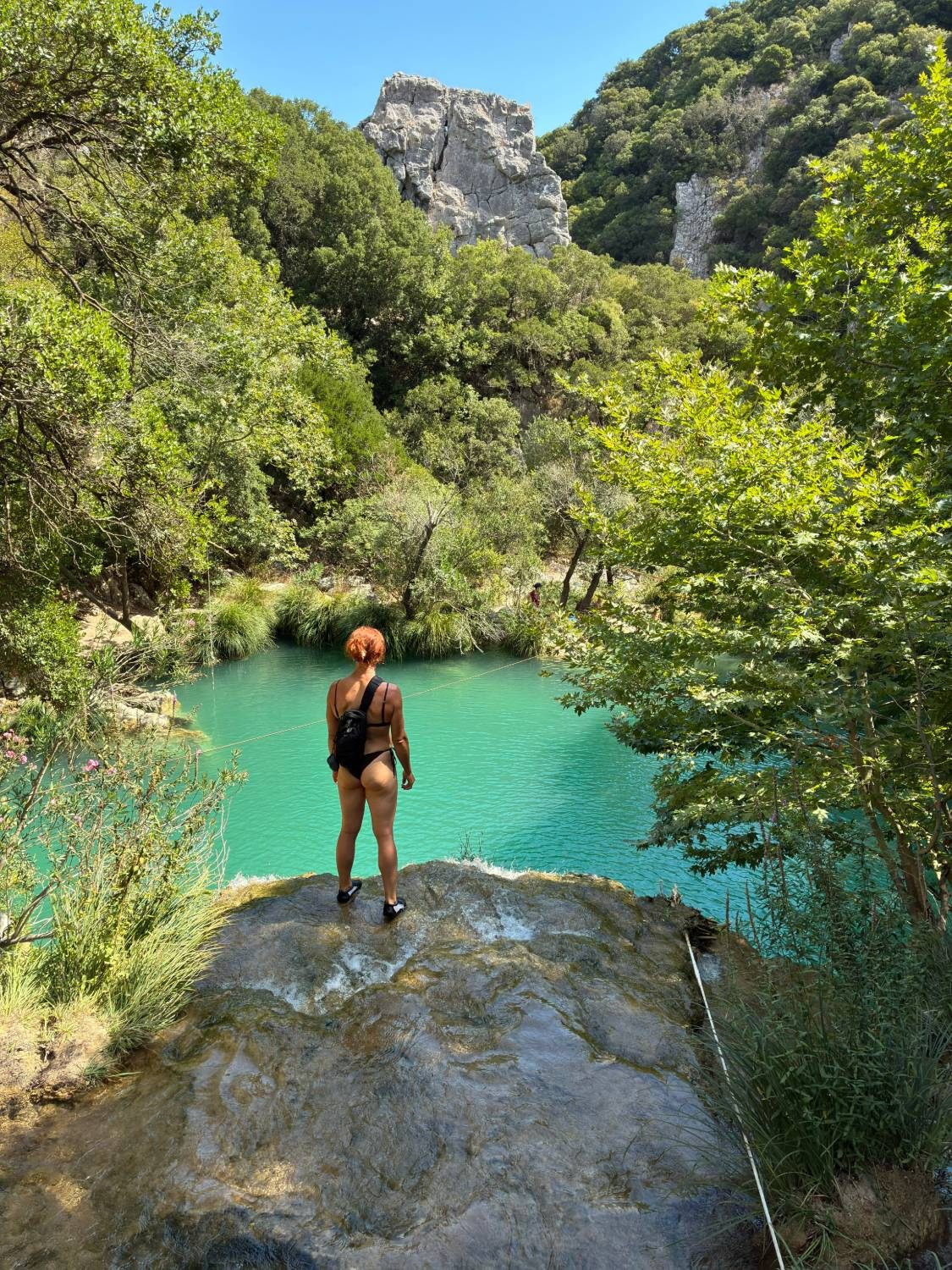 Kristine on top of Kadi Waterfall above a turquoise pool at Polylimnio