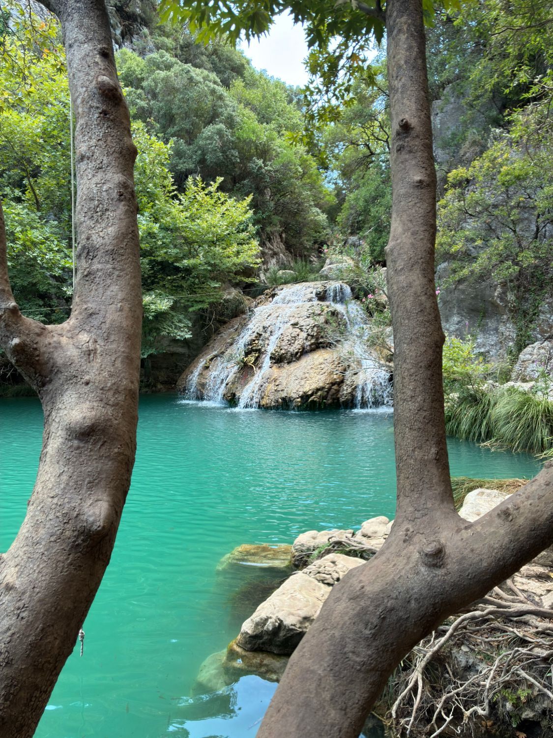 Kadi Waterfall and its turquoise pool at Polylimnio, framed between two tree trunks