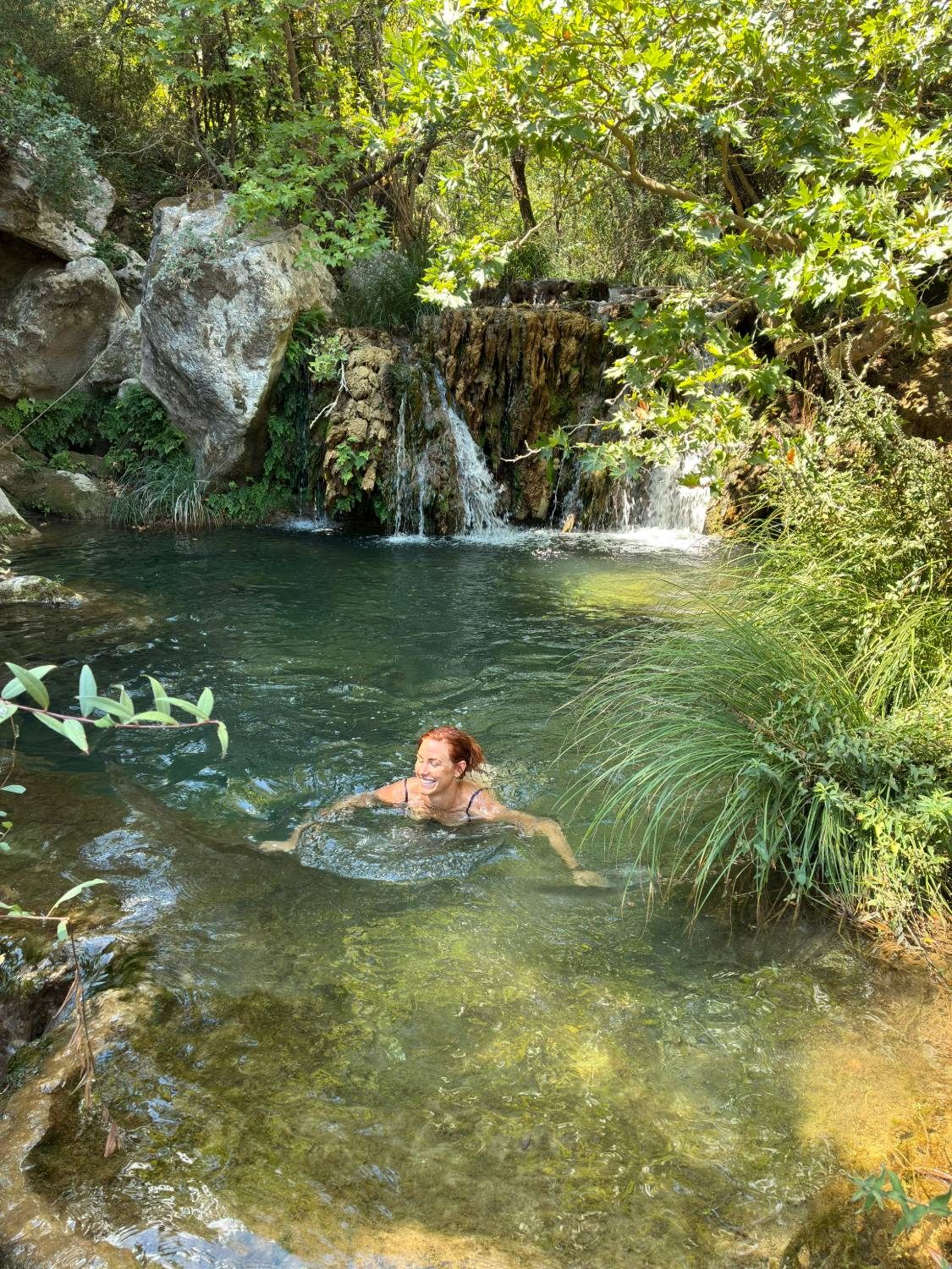 Kristine laughing as she swims in a clear green pool in front of a small waterfall